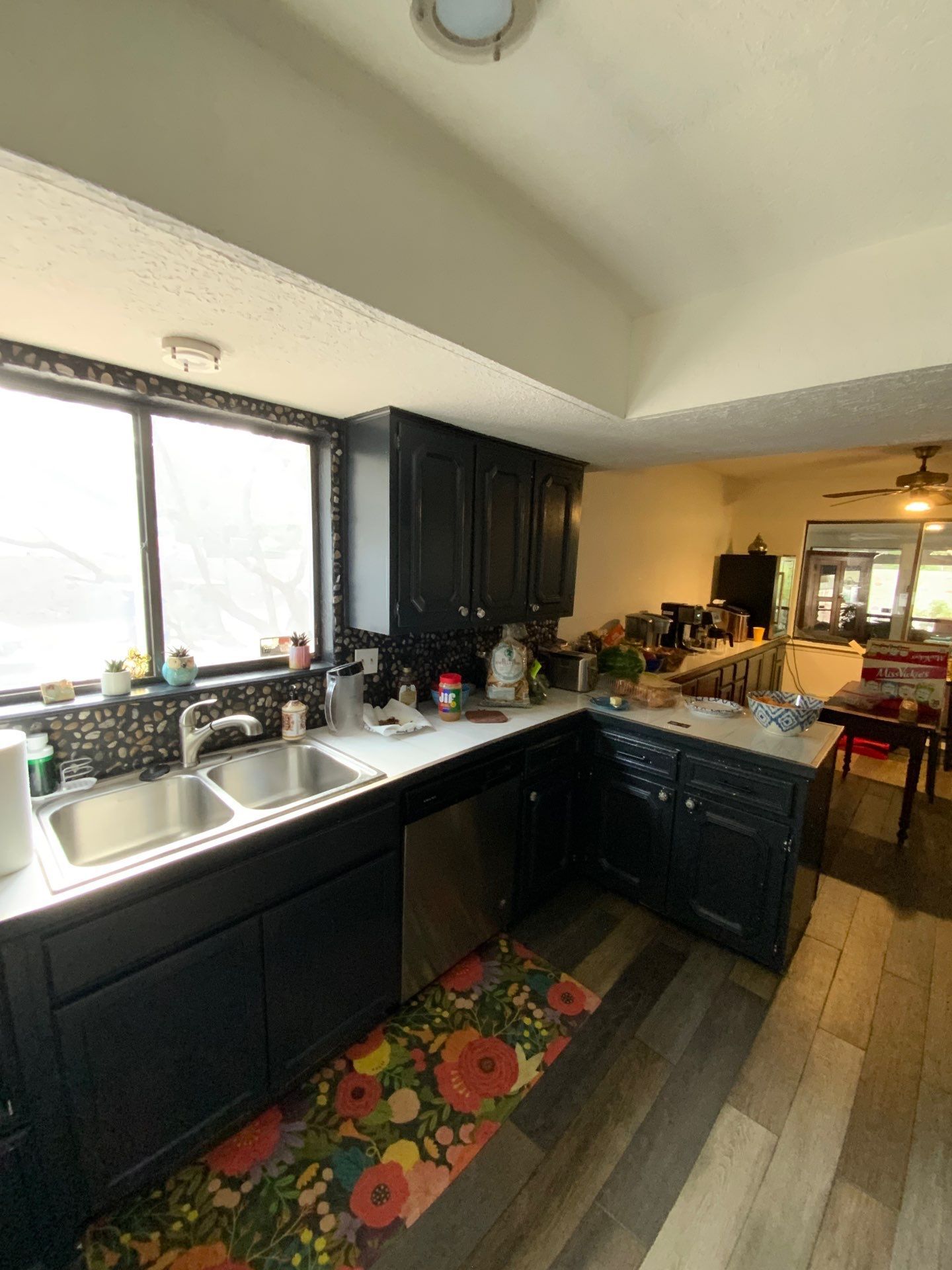 Modern kitchen with black cabinets, white countertops, a large window, and a dining area beyond