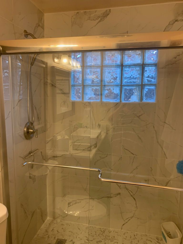Shower with glass door, marble-patterned tile, and a glass block window above.