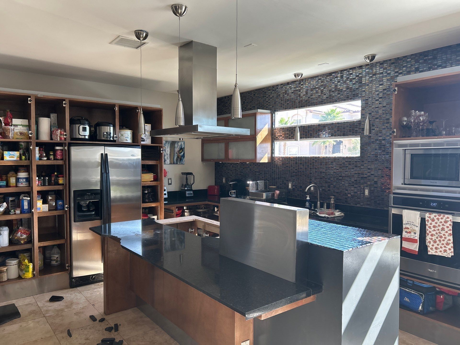 Kitchen with stainless steel appliances, dark countertops, open shelving, and a black tile backsplash.