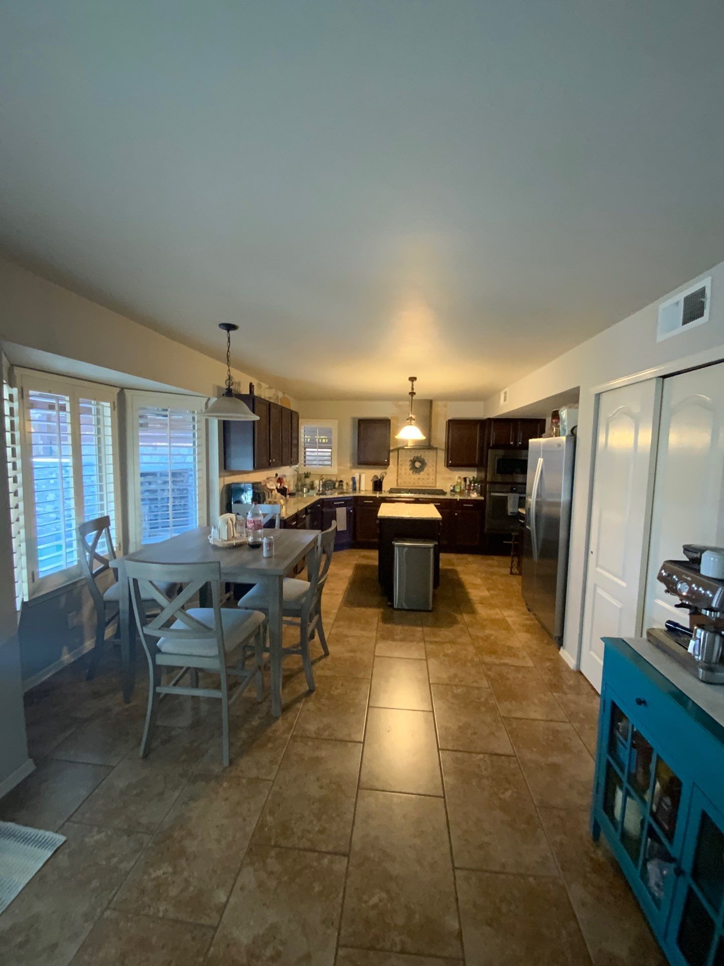 Open kitchen and dining area with tiled floor, island, and chairs, warmly lit in a home interior