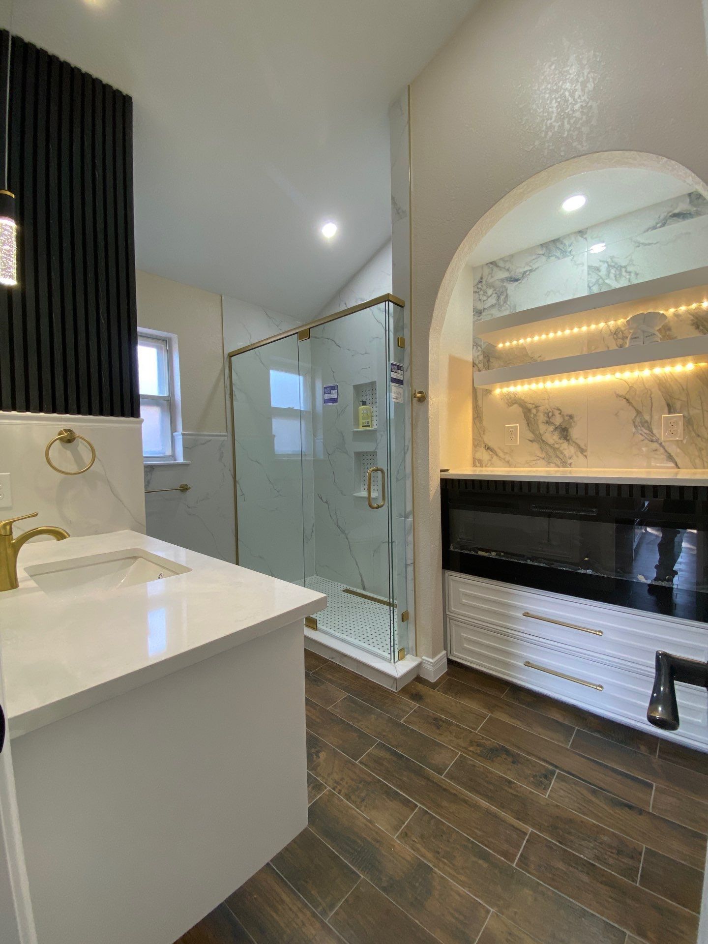 Bathroom with white vanity, marble accents, glass shower, and wood-look tile.