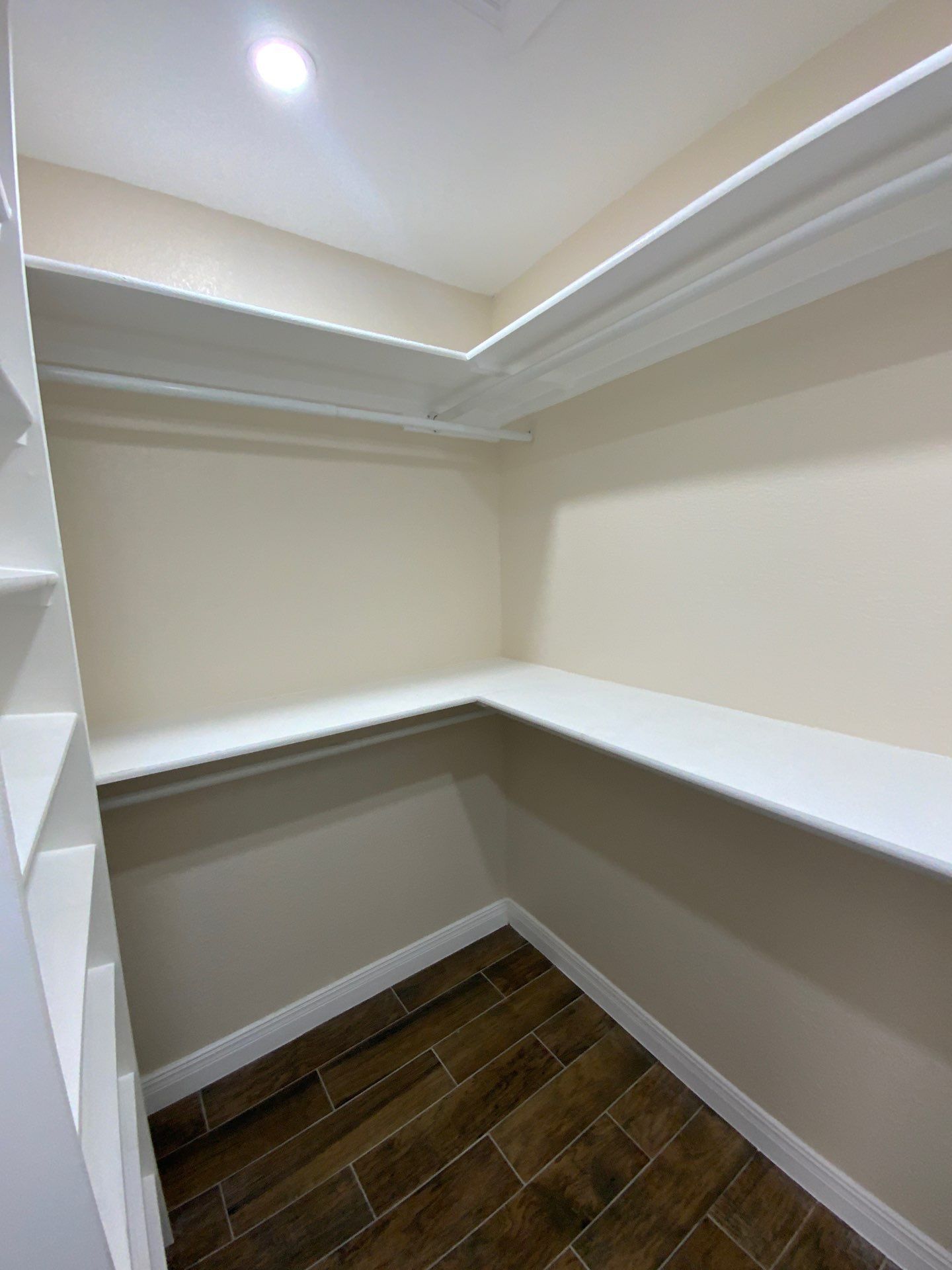 Empty white-shelved closet with wood-look tile floor and cream-colored walls.