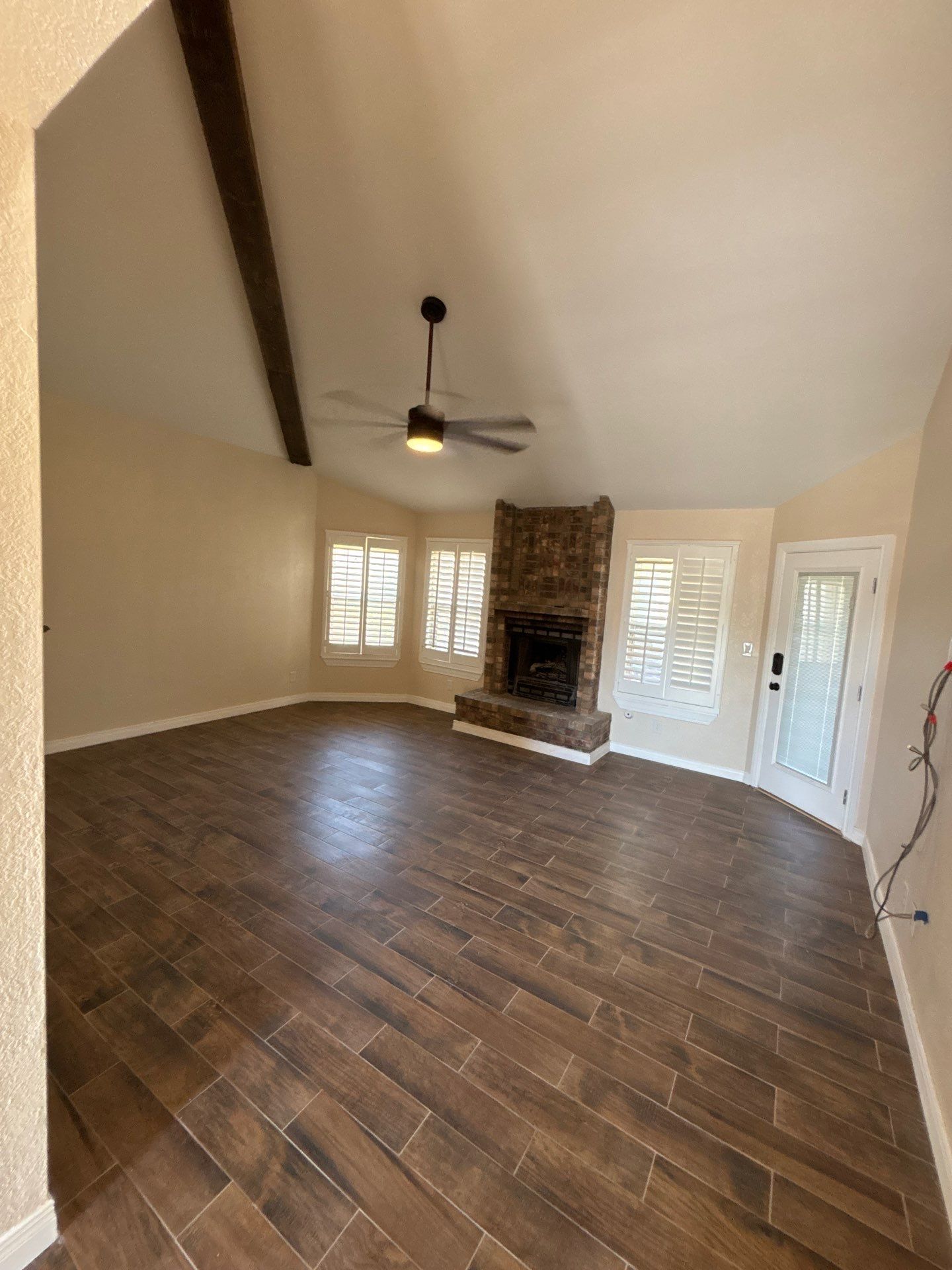 Empty living room with wood-look tile floors, fireplace, and a ceiling fan.