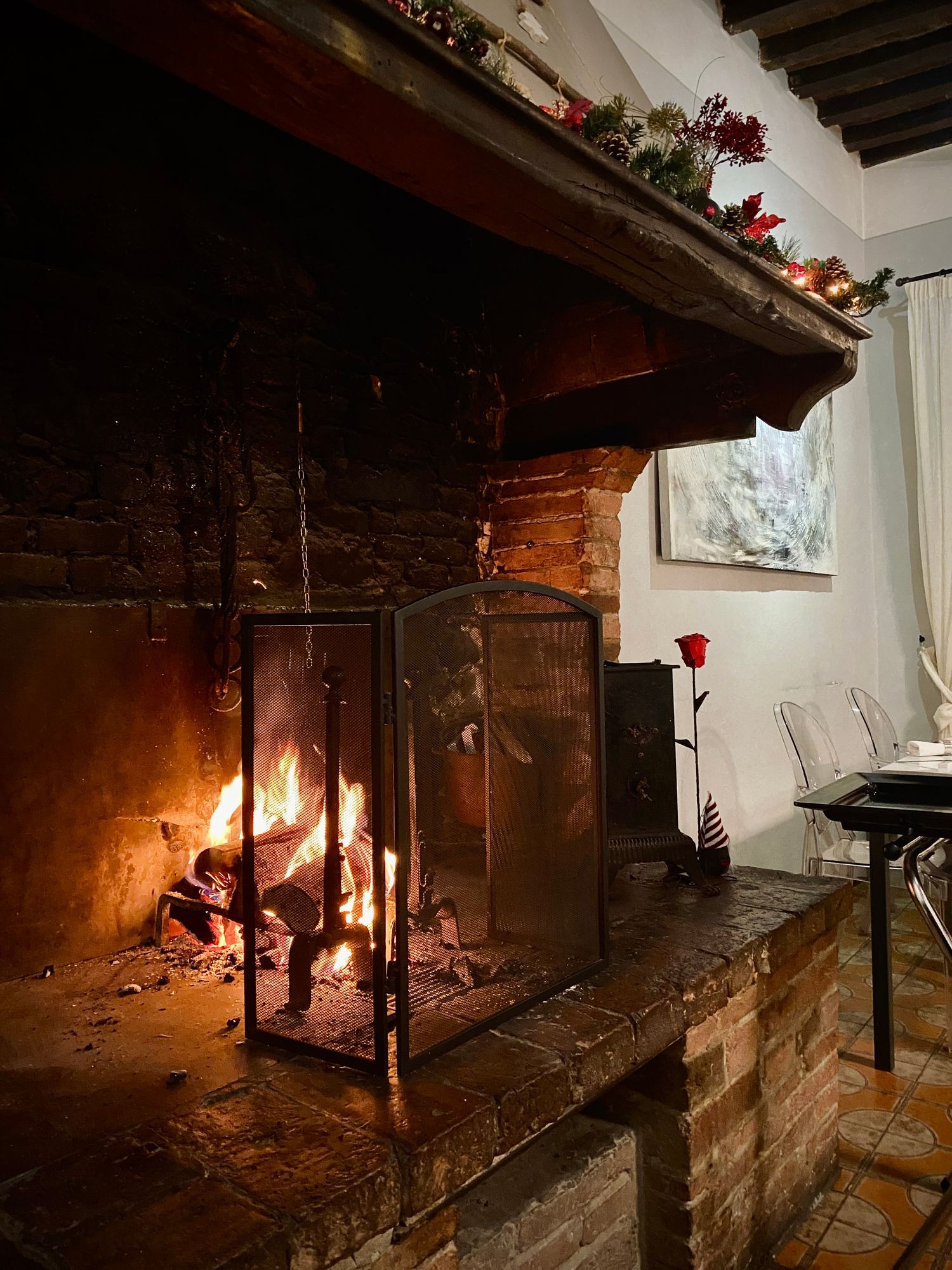 Un camino acceso con parascintille in metallo e mensola scura decorata con fiori, situato in una sala da pranzo in stile rustico.