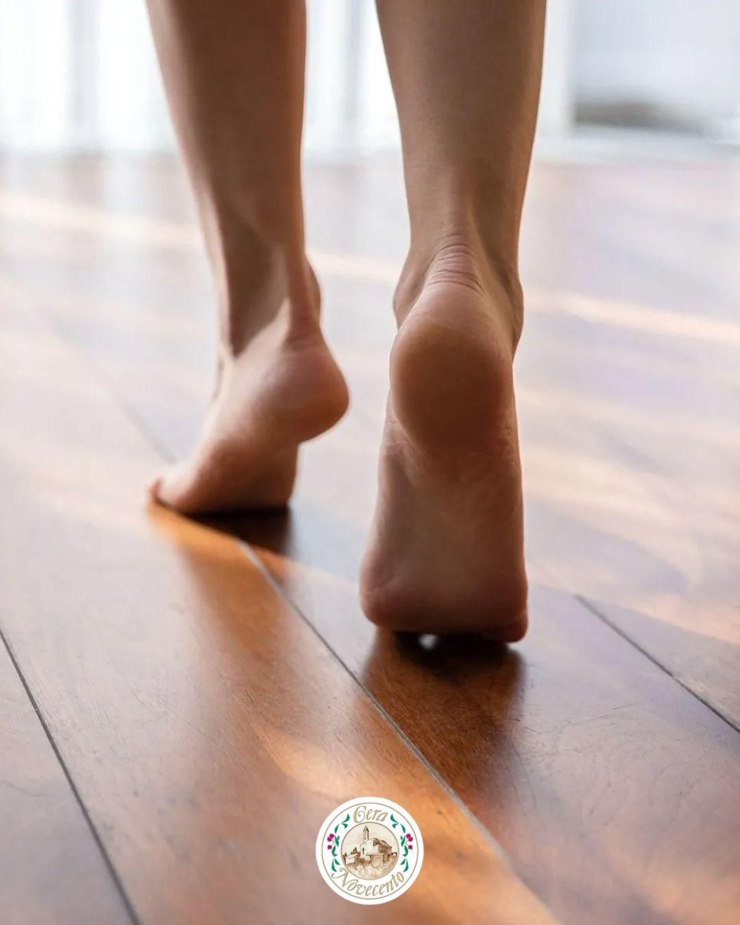 Piedi nudi che camminano su un pavimento di legno, con un piede sollevato a metà passo.