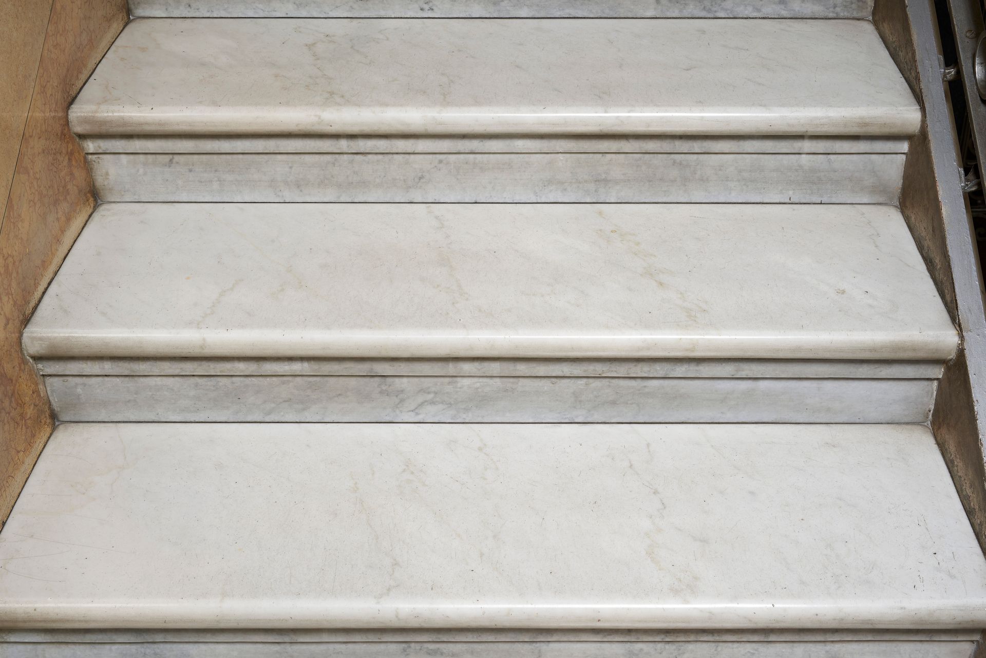 Tre gradini in marmo beige con bordi arrotondati, che scendono dal centro superiore verso il basso.