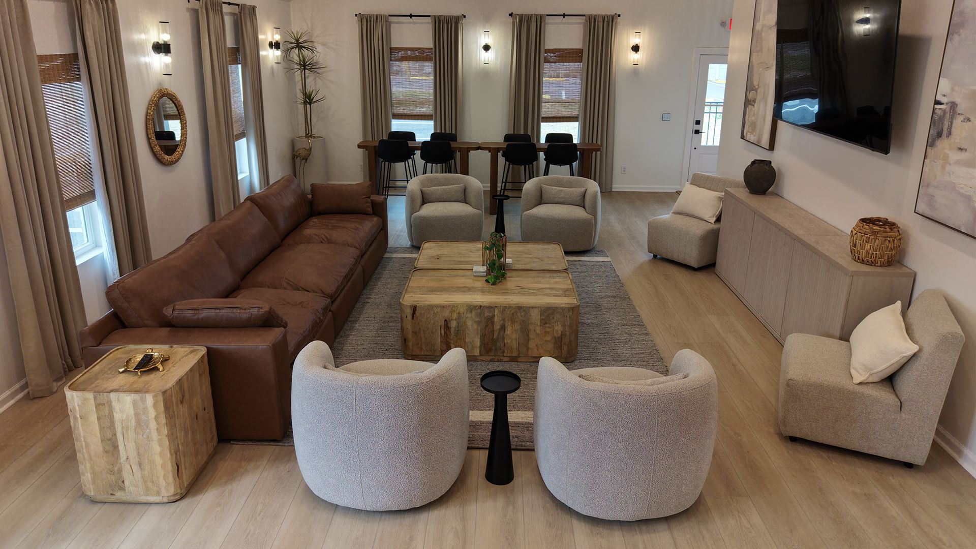 Lounge with a leather sofa, round cream armchairs, and wood coffee tables, with a bar table by the windows