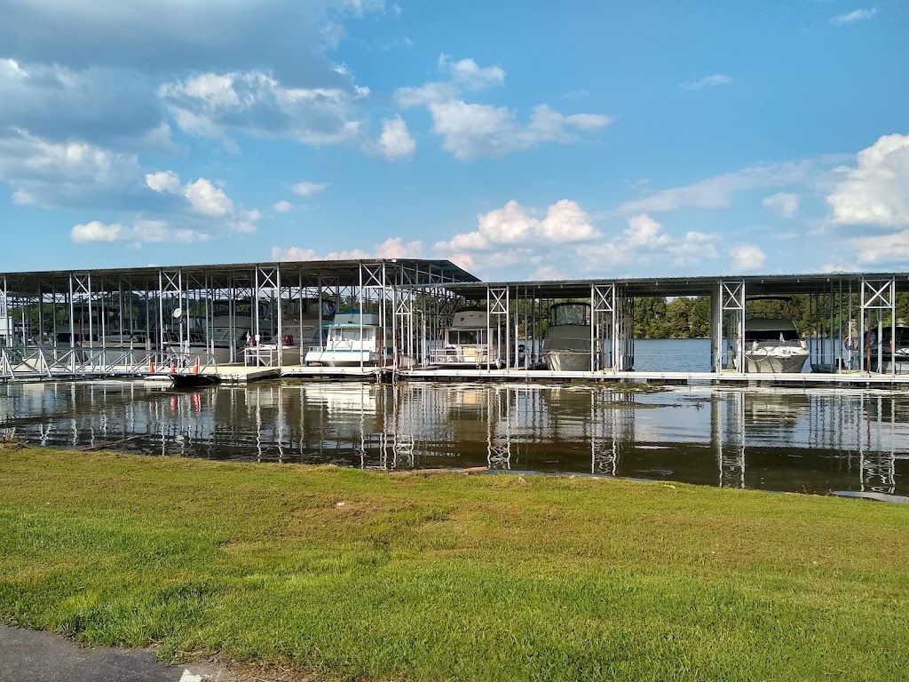 Covered boat docks with boats in their slips, seen from the grassy shore under a blue sky