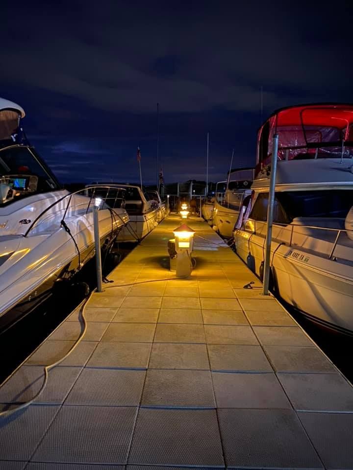 A row of boats are docked at a marina at night.