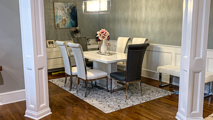 A dining room with a table and chairs and a rug on the floor.