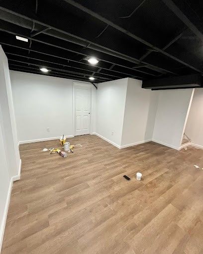 An empty basement with hardwood floors and white walls.
