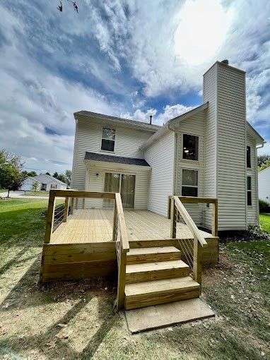 A white house with a wooden deck and stairs in front of it.