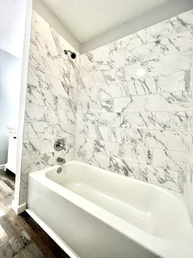 There is a bathtub in the bathroom with marble tiles on the wall.