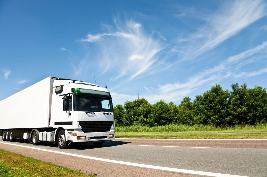 Un camion bianco che percorre un'autostrada sotto un cielo azzurro con nuvole.