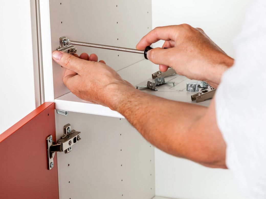 Mani che regolano una cerniera all'interno di un mobile da cucina bianco.
