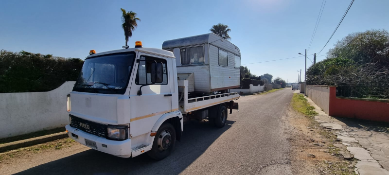 Un carro attrezzi bianco trasporta un rimorchio lungo una strada sterrata.