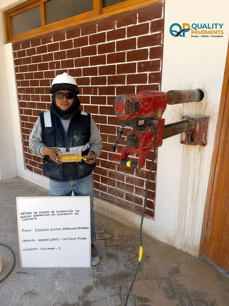 Un trabajador con casco sostiene un dispositivo junto a una pared de ladrillos y un equipo de prueba instalado.