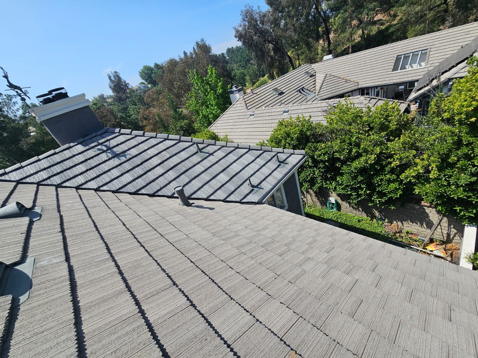Gray tile roofs on houses, surrounded by green trees and foliage under a bright blue sky.