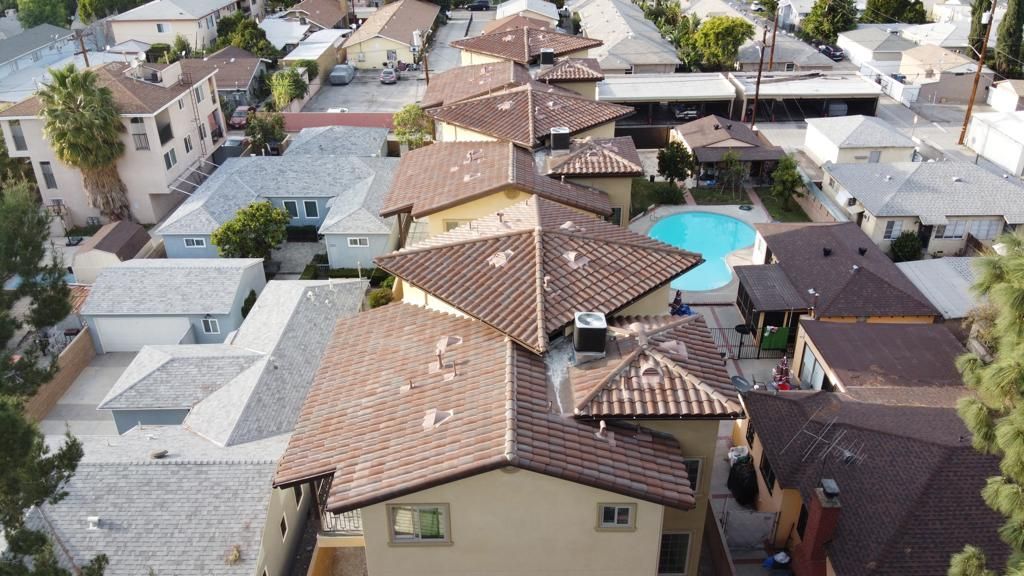 An aerial view of a neighborhood with tan houses, brown tile roofs, and a blue pool.