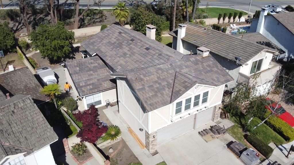 Aerial view of a beige two-story house with a tile roof, two-car garage, and a landscaped yard.