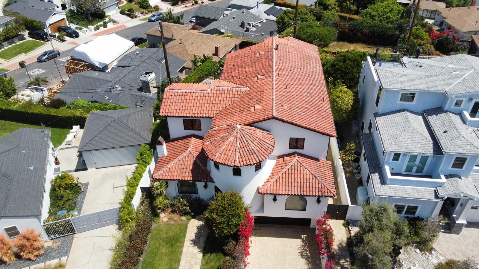 Aerial view of a Spanish-style house with a red-tiled roof, flanked by smaller houses and green trees.