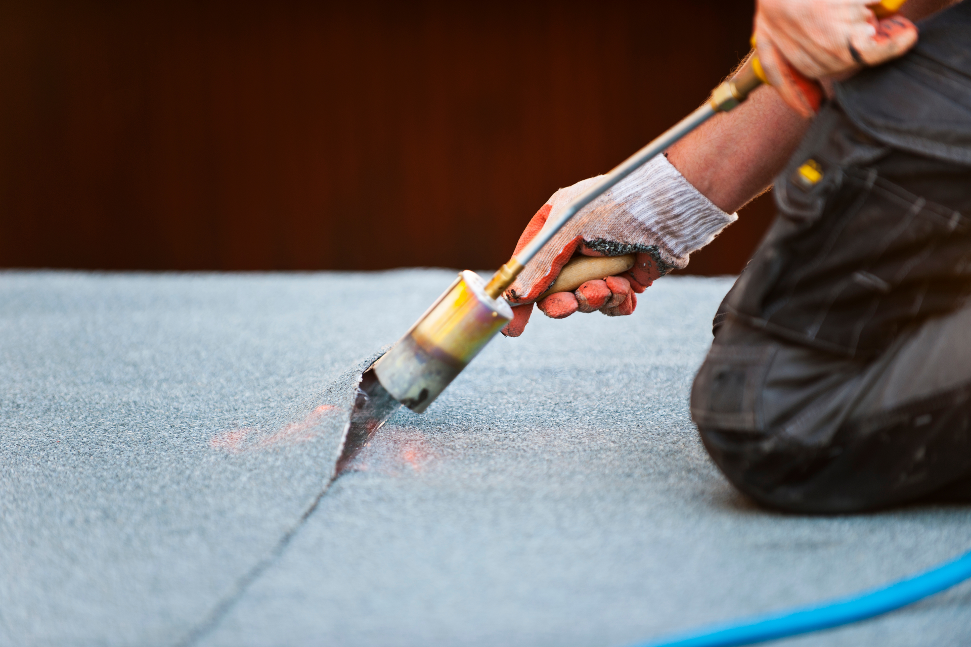 Person in work gloves welding a seam on a black rooftop with a torch.