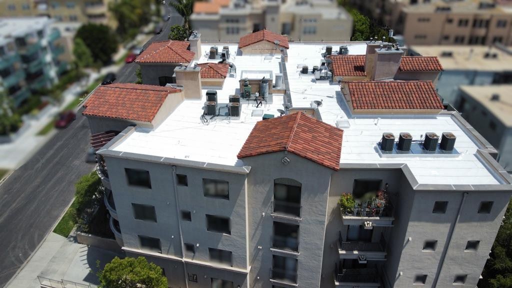 Multi-story apartment building with white walls and red-tile roof; surrounded by city buildings and street.