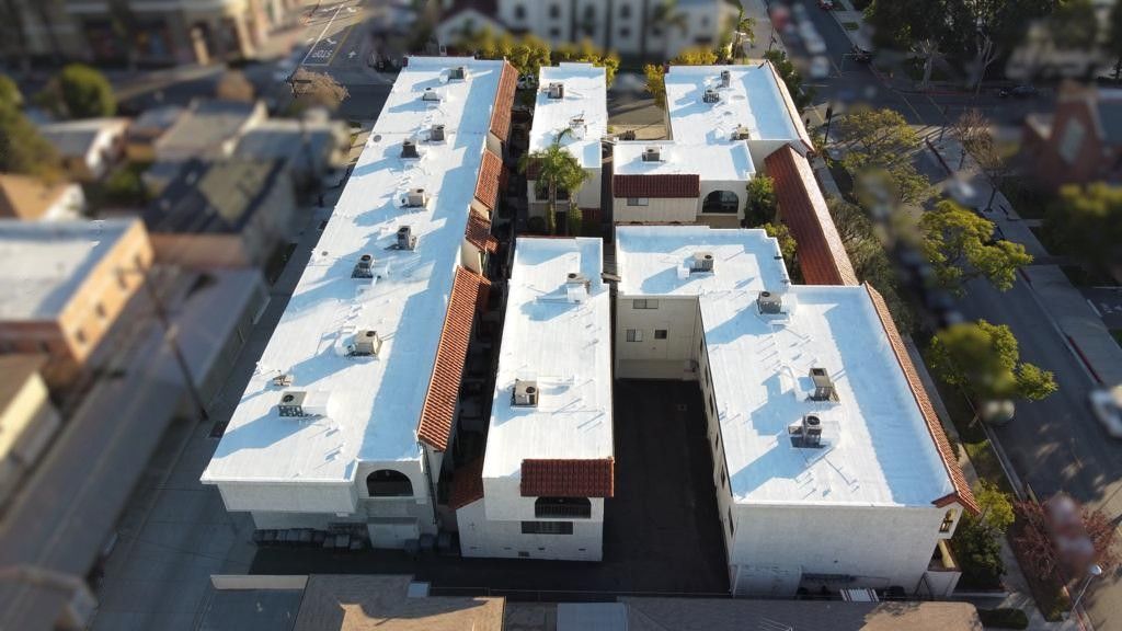 Aerial view of apartment buildings with white walls, red tile roofs, and parked cars below.