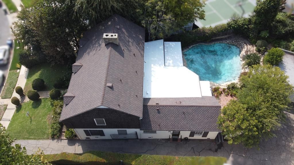 Aerial view of house with dark roof, pool, and surrounding greenery.
