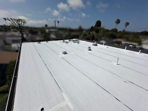 White flat roof on a building with vents and a blurred background of trees and sky.
