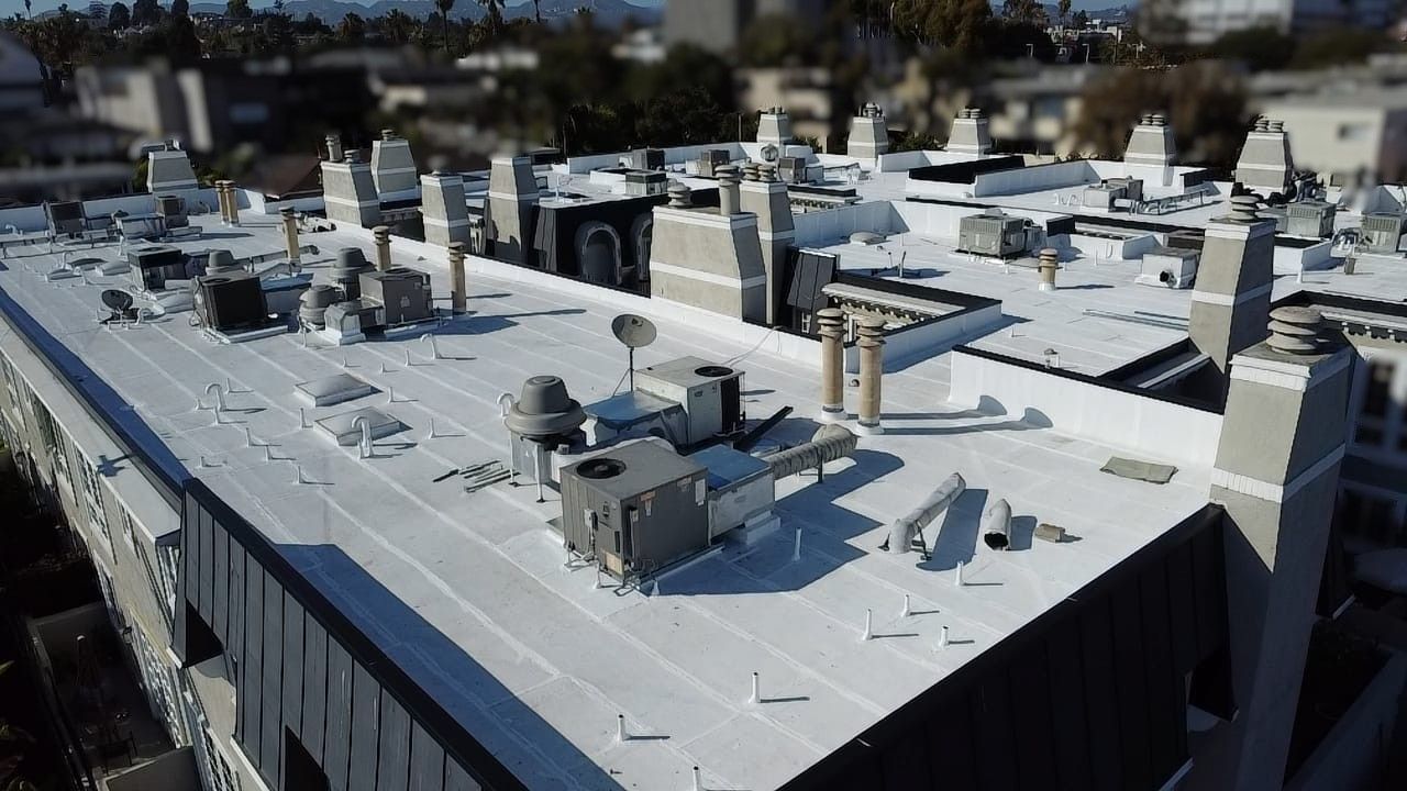 Rooftop of a building with white and grey structures, vents, and equipment. Sunny, daytime shot.