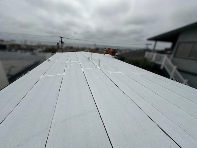 White painted flat roof of a building on an overcast day, with a residential neighborhood visible in the background.