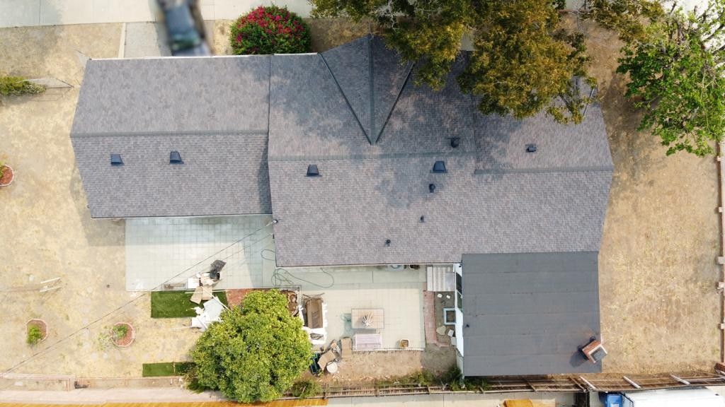 Overhead view of a house with gray roof, yard, and a car driving down the street.