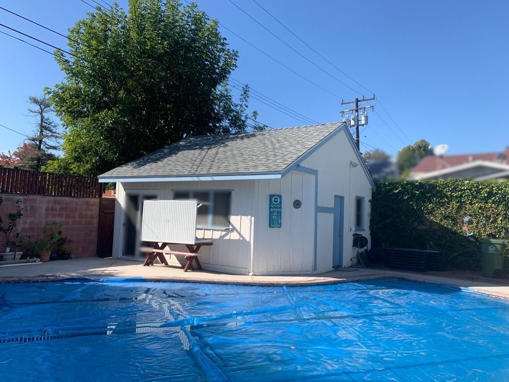A blue pool covered with a tarp, next to a white building with a picnic table.