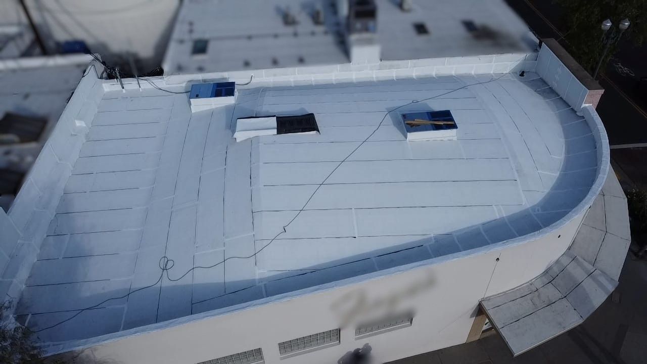 White building with a curved roof edge. Three square skylights are visible on the rooftop.