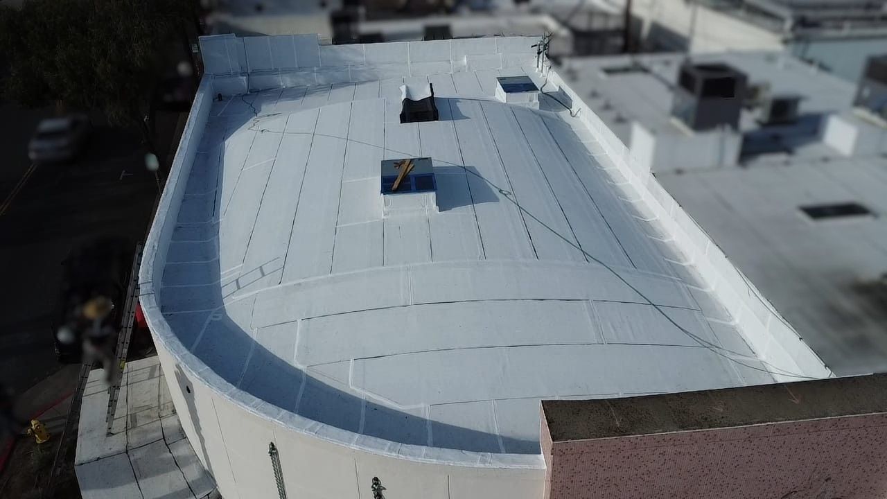 Overhead view of a white curved building roof with vents and surrounding buildings.