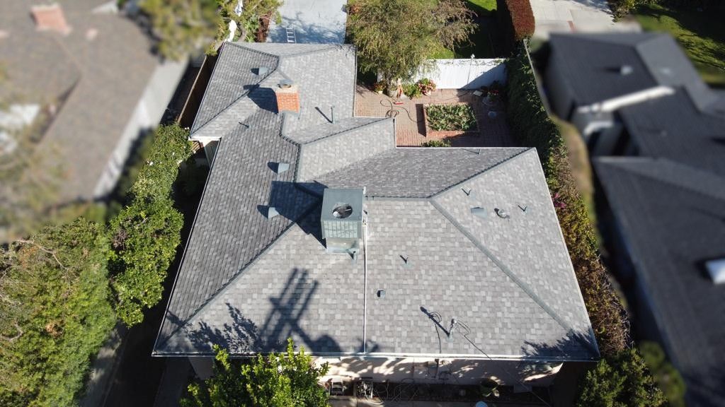 Overhead view of a house with a grey shingled roof, chimney, and surrounding greenery.