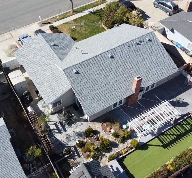 Aerial view of a house with a gray roof, a brick chimney, and a landscaped yard with a pergola.