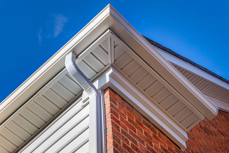 Corner of a building with white trim, gutters, and a brick wall, set against a bright blue sky.