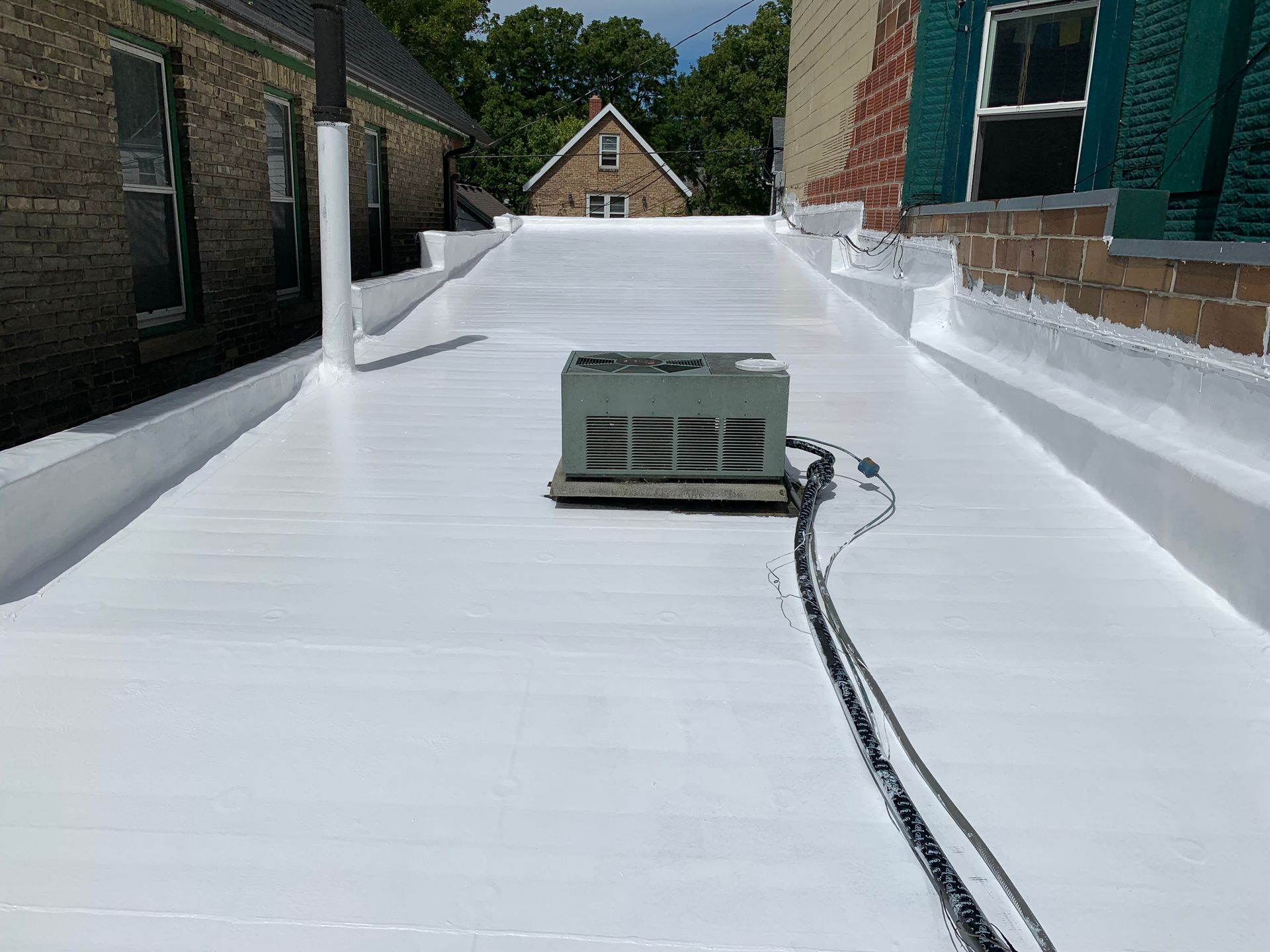 White flat roof with HVAC unit, between brick buildings, sunny day.