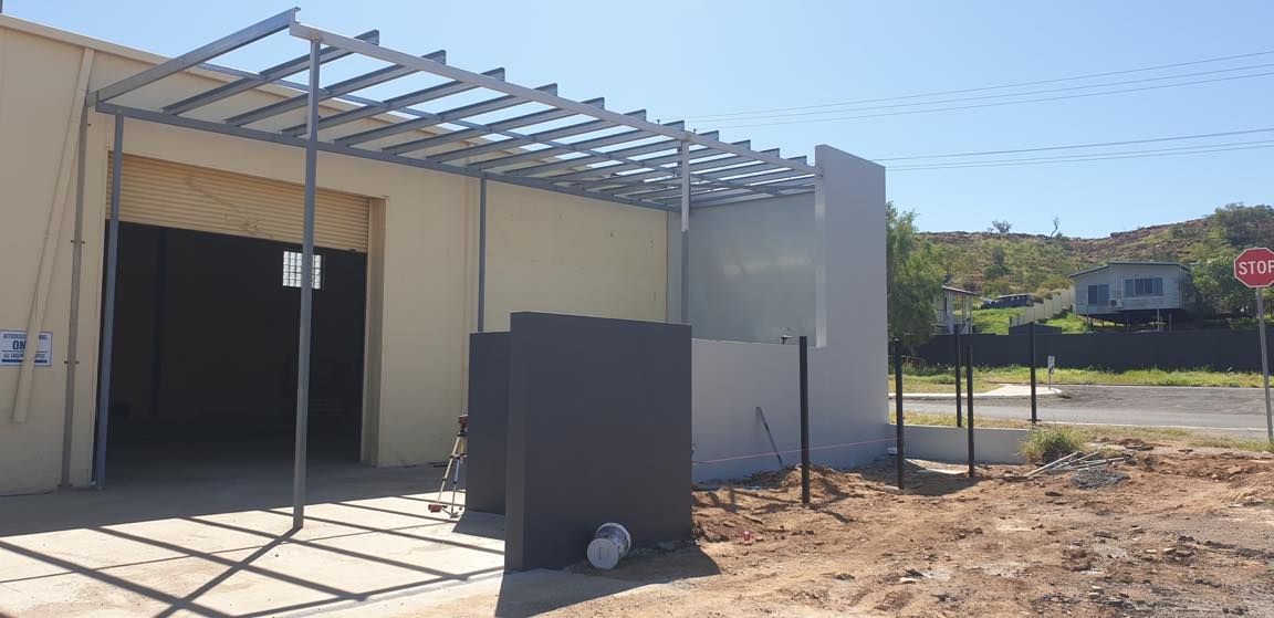 A Tan Building With A Metal Awning And An Open Garage Door — Custom Steel Fab in Garbutt, QLD
