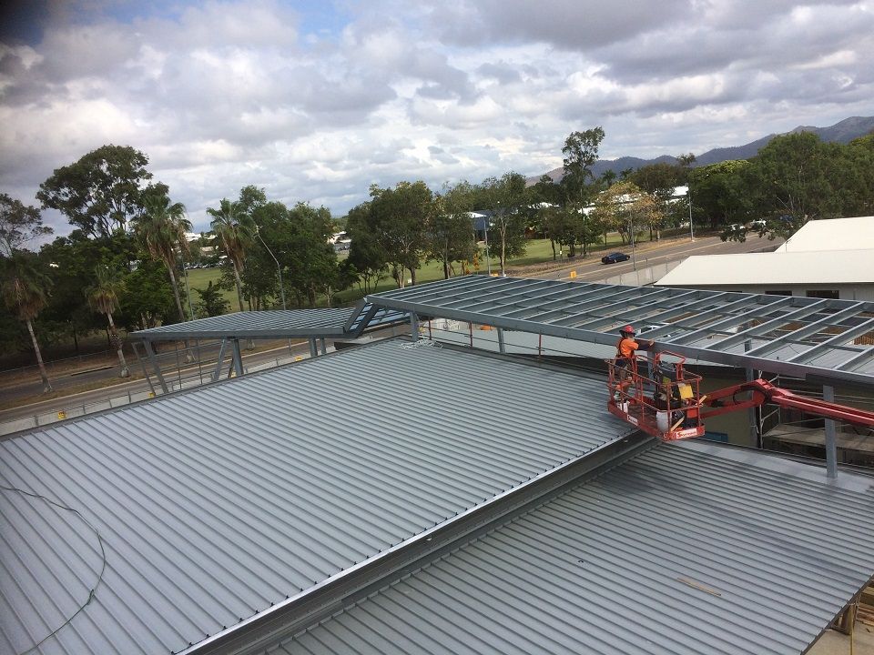 Construction Worker In Orange Lift On Metal Roof Under A Cloudy Sky — Custom Steel Fab in Garbutt, QLD
