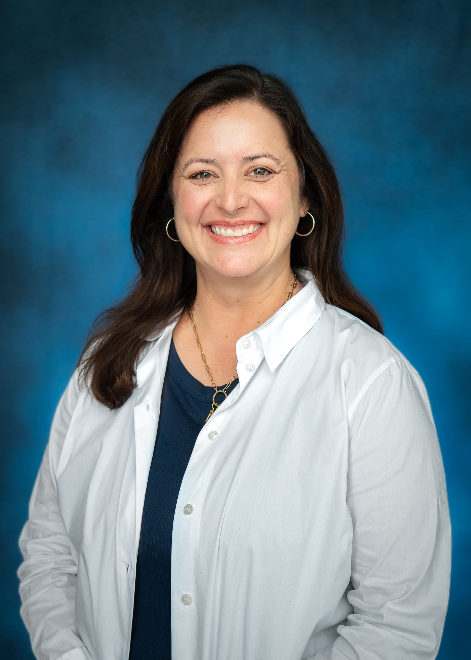 Woman in white shirt with a navy top smiling in front of a blue backdrop.