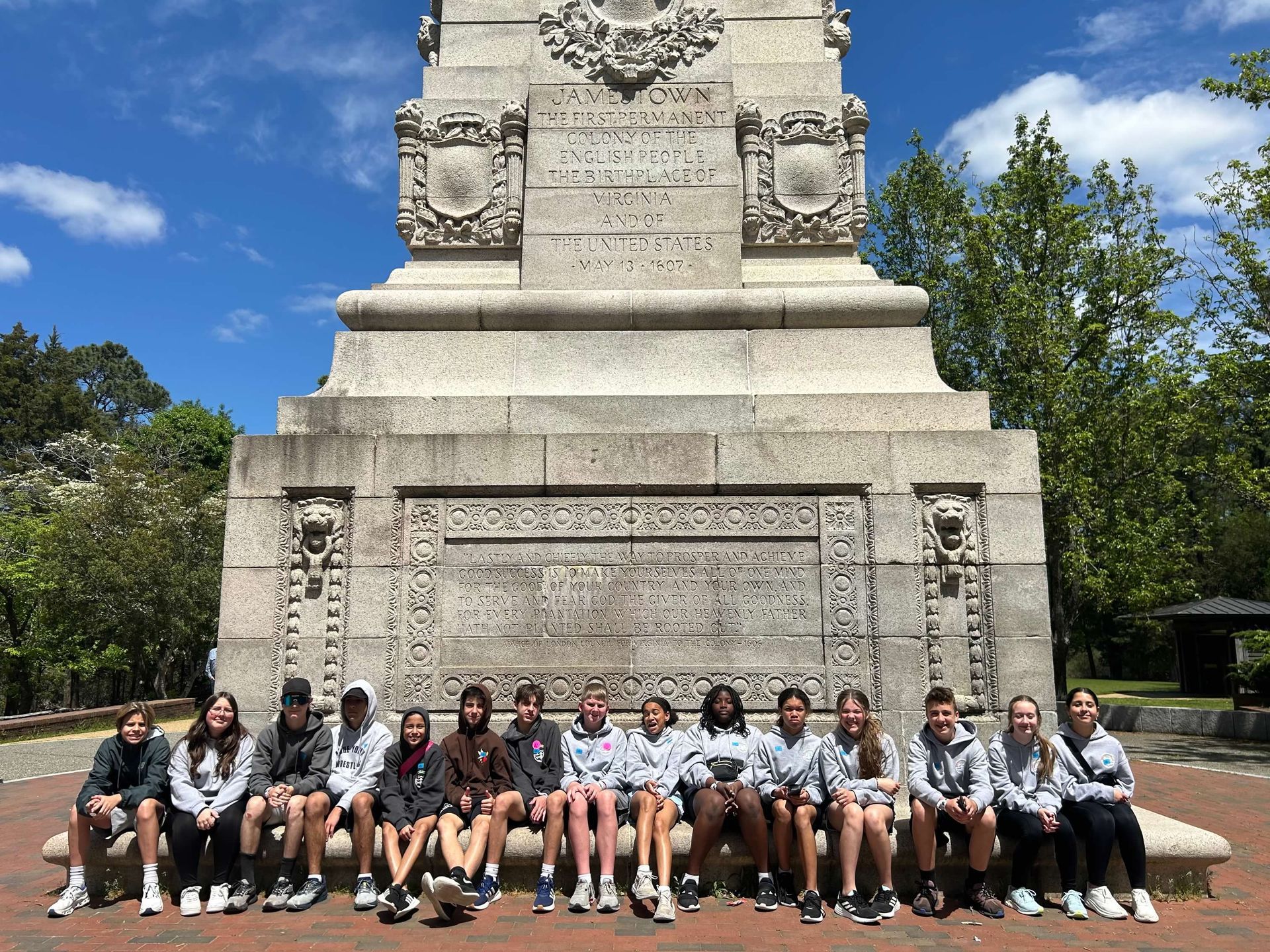 Group of people sitting in front of a stone monument on a sunny day.