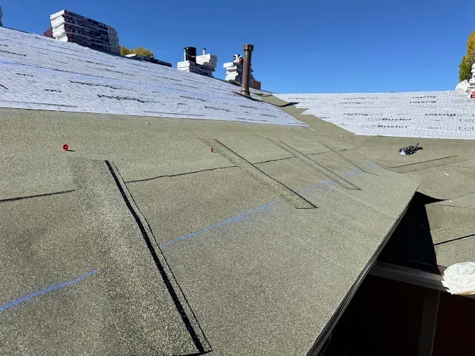 Partially repaired shingled roof with exposed underlayment and a small opening near the eave