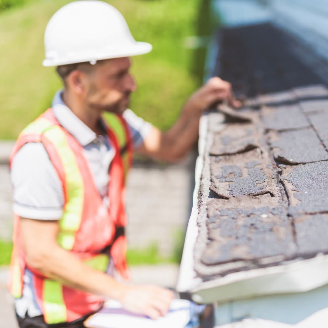 Construction worker in hard hat and safety vest inspecting roof shingles at a house