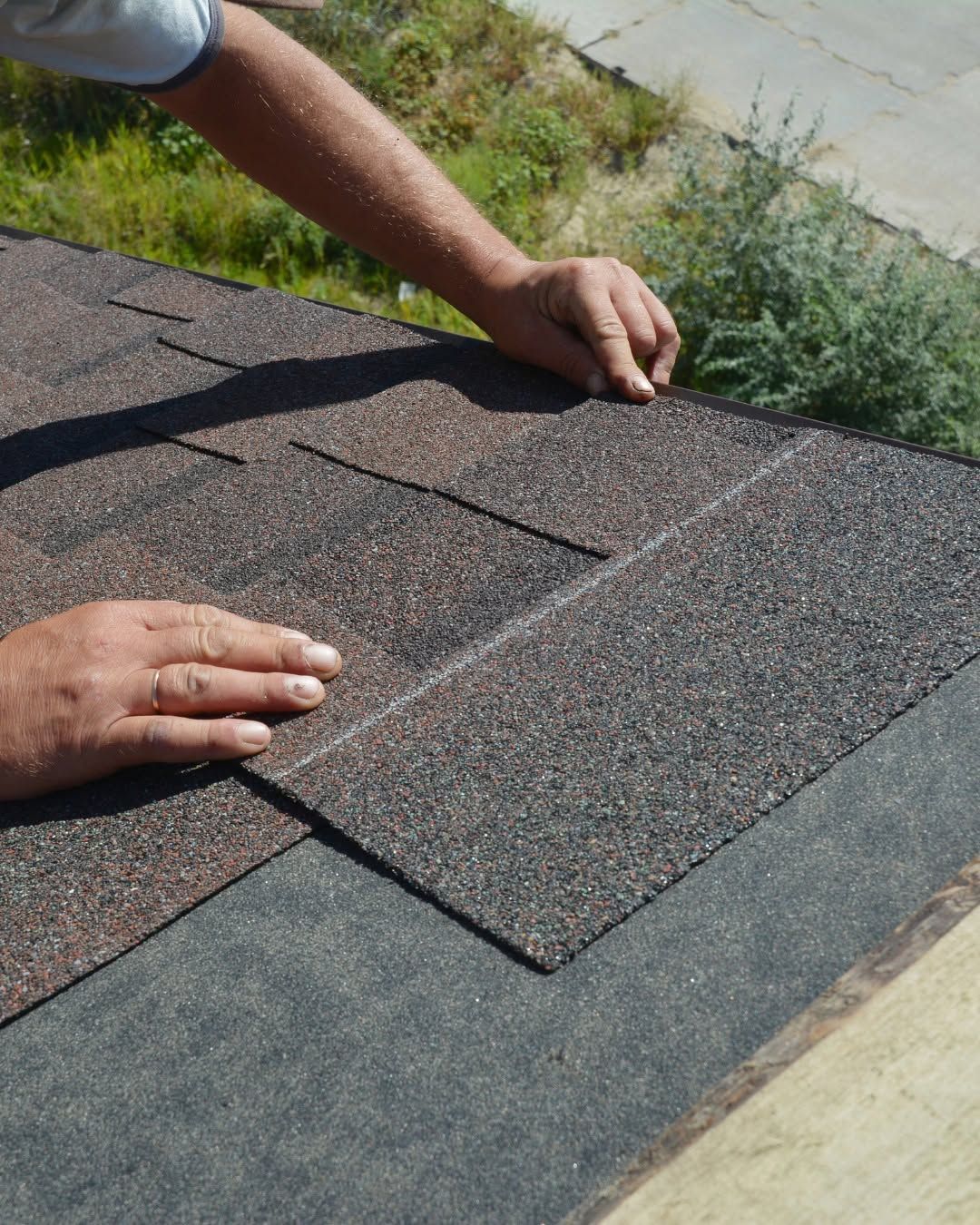 Hands installing asphalt roof shingles on a rooftop edge