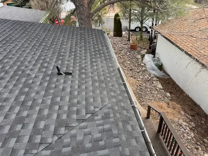 Roof shingles with a visible crack near the ridge, viewed from above beside a house and yard.