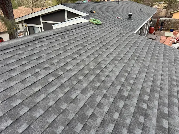 Roof with gray asphalt shingles and a green tool near the ridge, viewed from above.