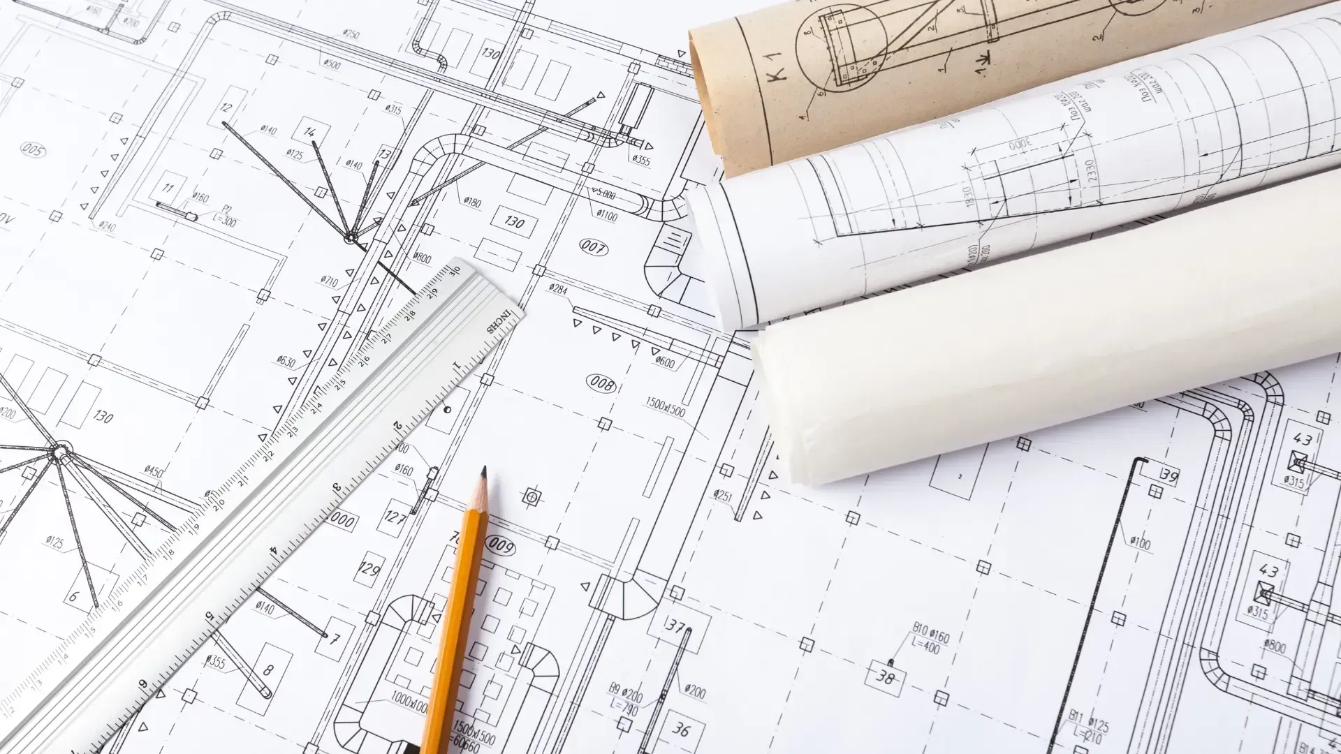 A pencil , ruler , and rolls of blueprints on a table.